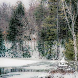 Tucked away along a riverbed, a lone cabin peeks out between the wintry branches.