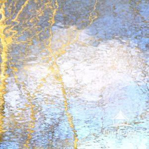 Reflection of blue sky and clouds with tree branches in small stream in Pennsylvania in winter.