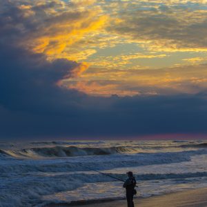 Lone surf fisherman braves the surf & cold of a late fall sunset.