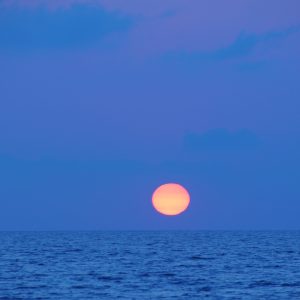 Golden sun approaching the horizon against blue backdrop.  Falerna, Italy.