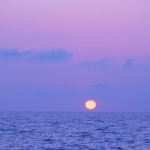 The golden sun going down against purple sky and background. View from Falerna Marina, Calabria -