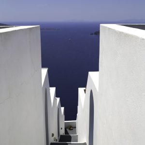Pretty white alley heading downwards to the gorgeous blue waters of the island of Santorini, Greece.