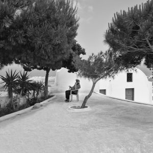 Old man sitting under trees, relaxing from the summer heat. Santorini, Greece.