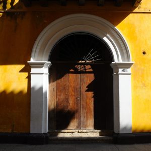 Afternoon sun and shadows hitting pretty yellow wall and arched wooden door in Cartagena, Colombia.