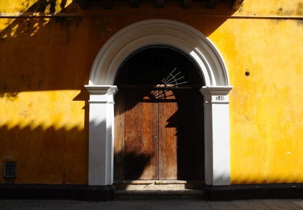 Afternoon sun and shadows hitting pretty yellow wall and arched wooden door in Cartagena, Colombia.