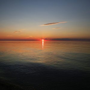 Sun just below a few clouds but before it goes down below the horizon.