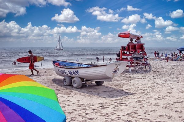 A beach scene of the Cape May lifeguard stand with lifeboat, The surfer walking on the beach with