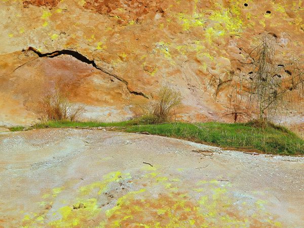 A rugged golden cliff face shows signs of erosion with a small cave-like opening and sparse