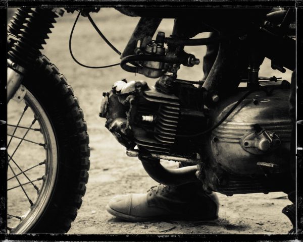 A motorcycle rider rests his foot on the ground while he revs up his engine.