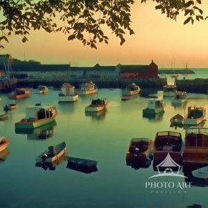The image shows a scenic depiction of Rockport Mass Harbor at sunset. The sky is displaying warm
