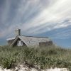 This photograph depicts a solitary house situated amidst tall grasses with a sandy foreground. The