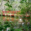The artwork is a vibrant painting of a red wooden bridge spanning across a calm body of water. The