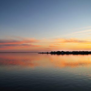 Beneath a pink-peachy and yellow sky, the tranquil waters mirror the ethereal beauty of dusk,