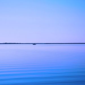 A serene blue-hued bay, where straight lines and gentle ripples frame a distant boat, creating a