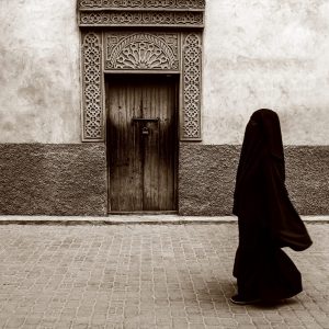 Captured against the backdrop of Marrakesh's ornate doorways, a veiled woman moves gracefully,