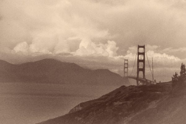 This is a sepia-toned photograph of the Golden Gate Bridge. The bridge stands prominently against a