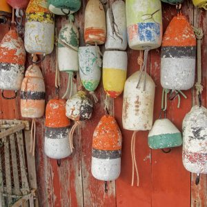 This photo is of an assortment of colorful lobster buoys hanging against a red background. The buoys