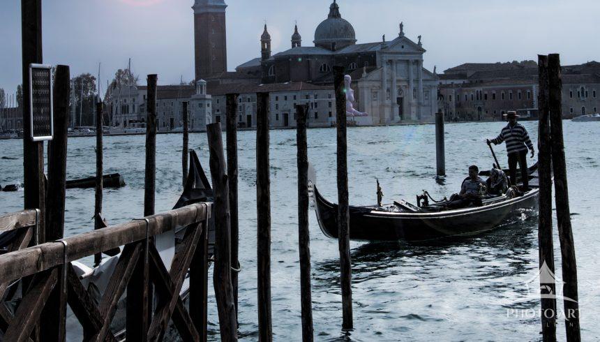 This is a serene scene of a Venetian canal at dusk. In the foreground, there are several wooden