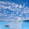This is a photograph of a serene seascape under a vast, expansive sky filled with scattered, fluffy