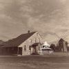 This sepia-toned photograph depicting the rustic, Gardner Mill Cottege Museum situated on its grassy