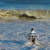 This photo depicts a dynamic ocean scene featuring a surfer, dressed in a wetsuit, standing in the