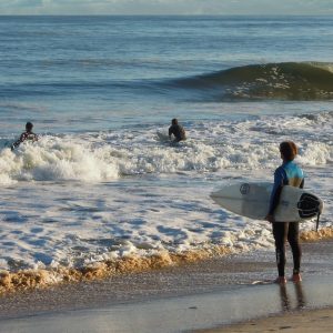 This photograph captures a serene beach scene during late afternoon. In the foreground, a surfer