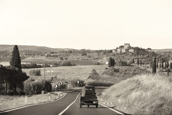 A charming APE truck cruises along a winding road through the picturesque Tuscan countryside. A