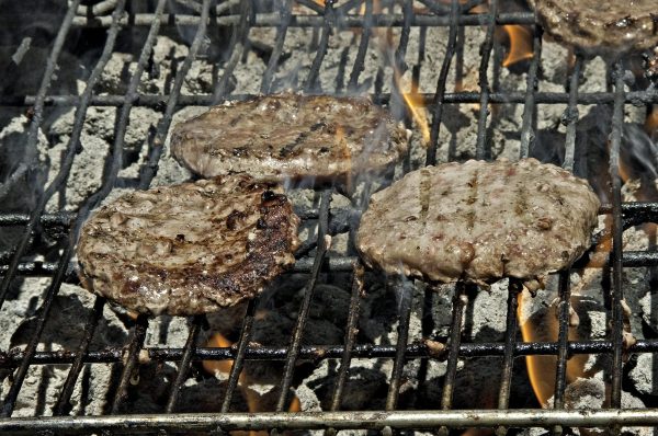 The BBQ grill is cooking three delicious hamburgers.