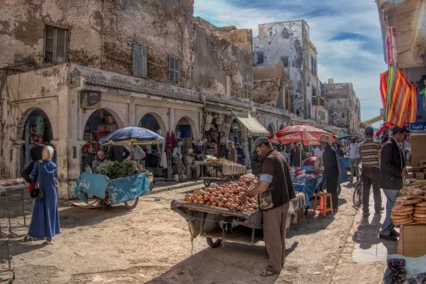 This image is a vibrant, detailed photograph capturing a bustling street market in Morocco. The