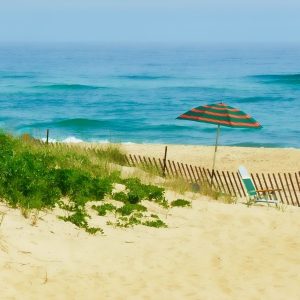 This is a photograph of a serene beach scene. The composition features golden sand dunes in the