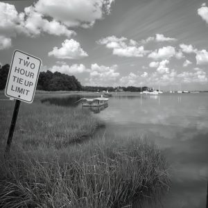 This black and white photograph captures a serene mooring pond scene. In the foreground, there is a