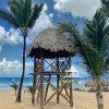 This photograph captures a tropical beach scene featuring a wooden lifeguard tower with a thatched