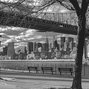 This black and white photograph is of the 59th St Bridge bridge and the skyline of a NYC. The