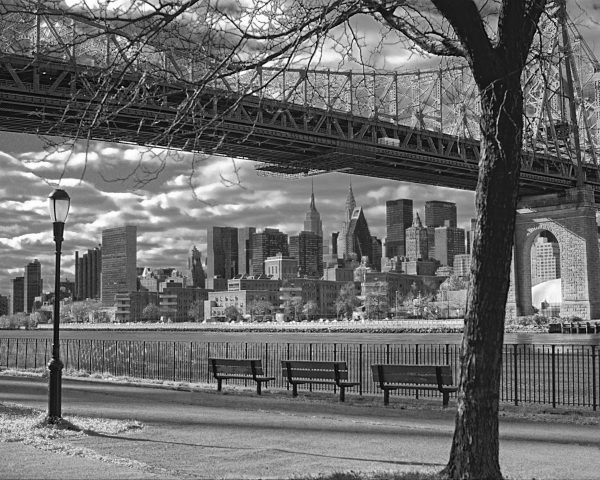 This black and white photograph is of the 59th St Bridge bridge and the skyline of a NYC. The
