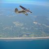 This photograph shows an aerial view of a small plane flying over the coastline of eastern Long