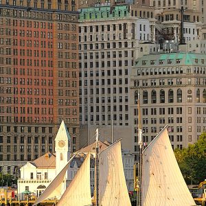 A sunlit sailboat in front of New York City buildings.