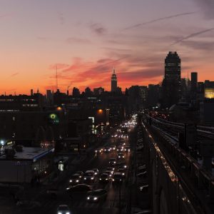 This panoramic photo depicts a busy urban scene in Long Island City. In the background is Manhattan