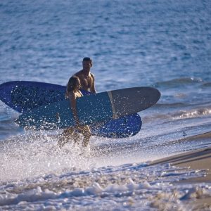 This is a photograph of a couple exiting the ocean after surfing. They are walking onto the beach
