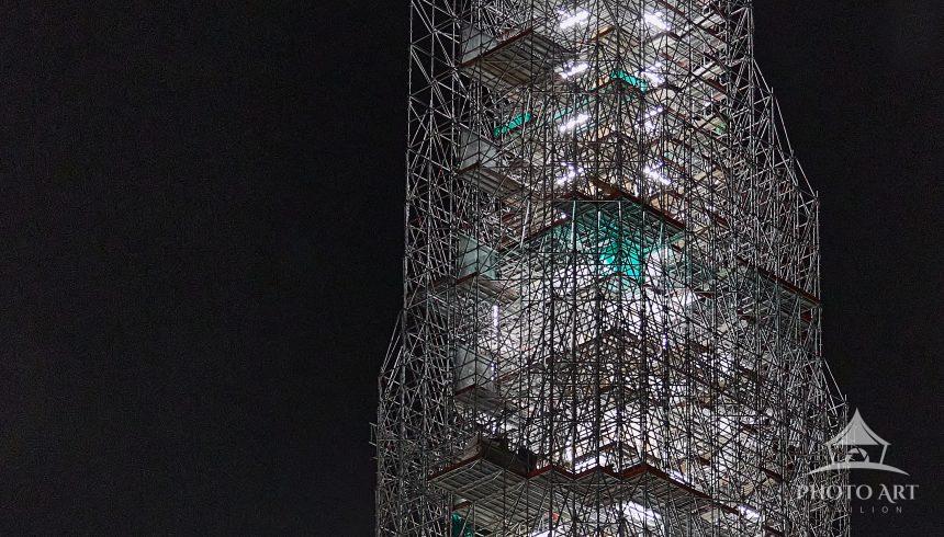 The spire scaffolding tops out in the darkness, but the work goes on 24/7.