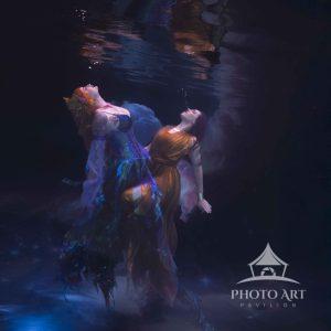 Beneath the tranquil surface of moonlit waters, two mermaids dancing in the moon light drift with a