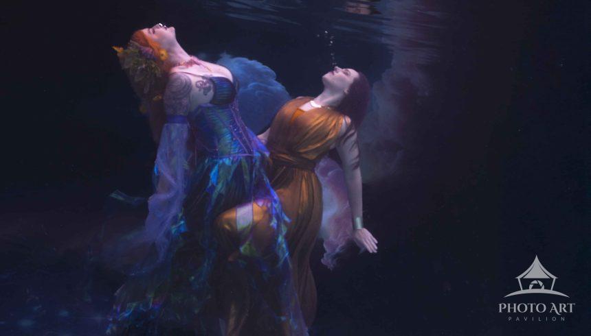 Beneath the tranquil surface of moonlit waters, two mermaids dancing in the moon light drift with a