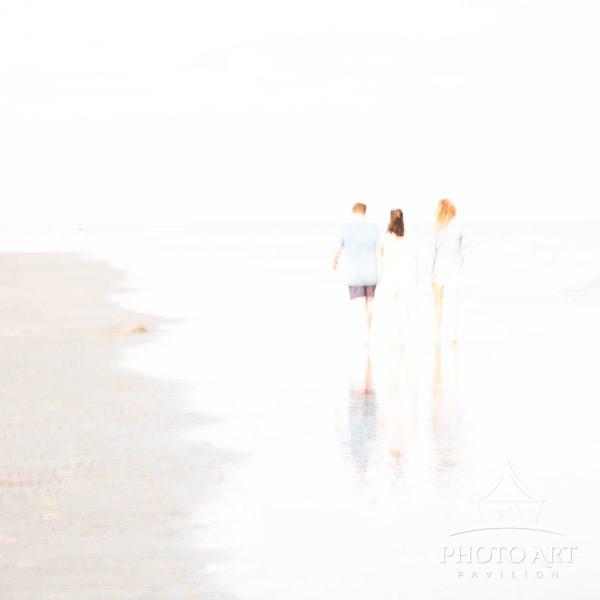Three friends strolling along the beach at low tide, as sunset approaches. Walking at the water's