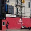 A dramatic bold red wall at a NYC bus stop punctuated by color and light, is furthered by a defunct