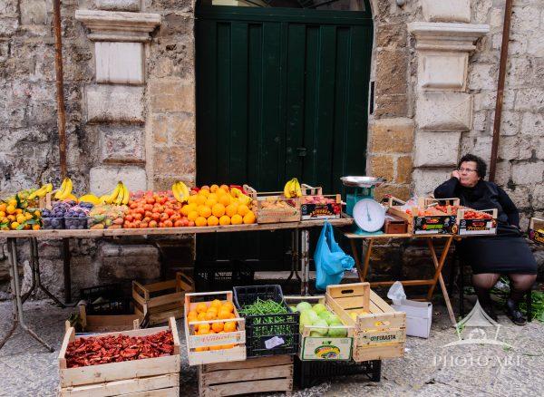 The artwork is a vibrant photograph depicting a street market scene with a rustic and textured stone