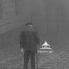 The artwork is a monochromatic photograph capturing an elderly person walking down a cobblestone