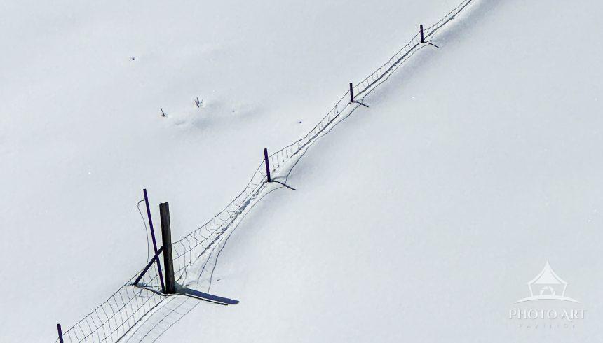 The snow depth obscures all landmarks except the fence line that leads the way home.