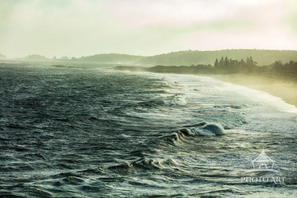 Low yellow light of sunset catches the raindrops & fog to recast a dark blue sea in a greenish hue.
