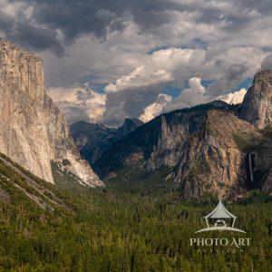 A stunning view of Yosemite's majestic mountains under a cloudy sky. The rich green of the forest