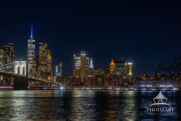 A sweeping nighttime view of Lower Manhattan rises above the East River, with the illuminated