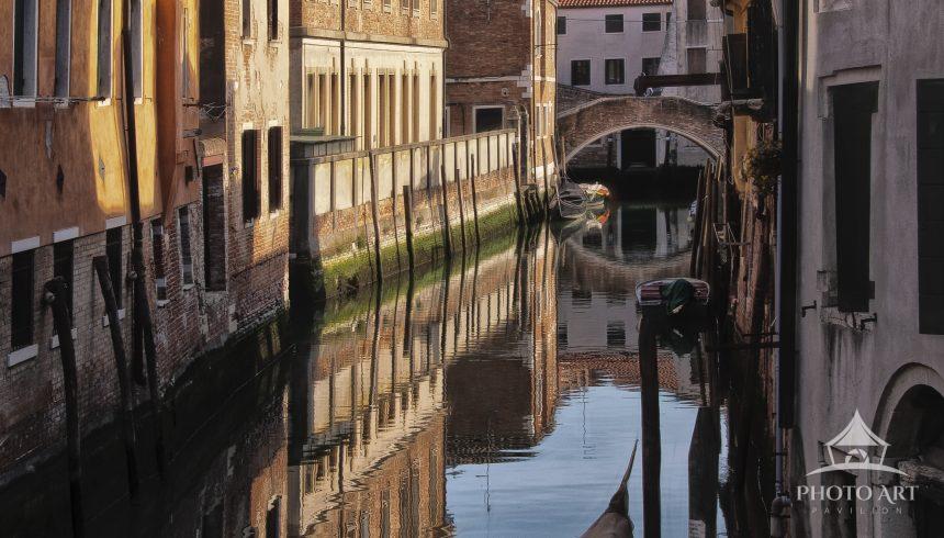 Lonely Canal in Venice presents a quiet moment along a narrow waterway. The image is framed by tall,